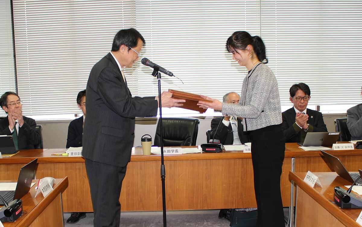 写真：永田学長から表彰楯を授与される粉川准教授